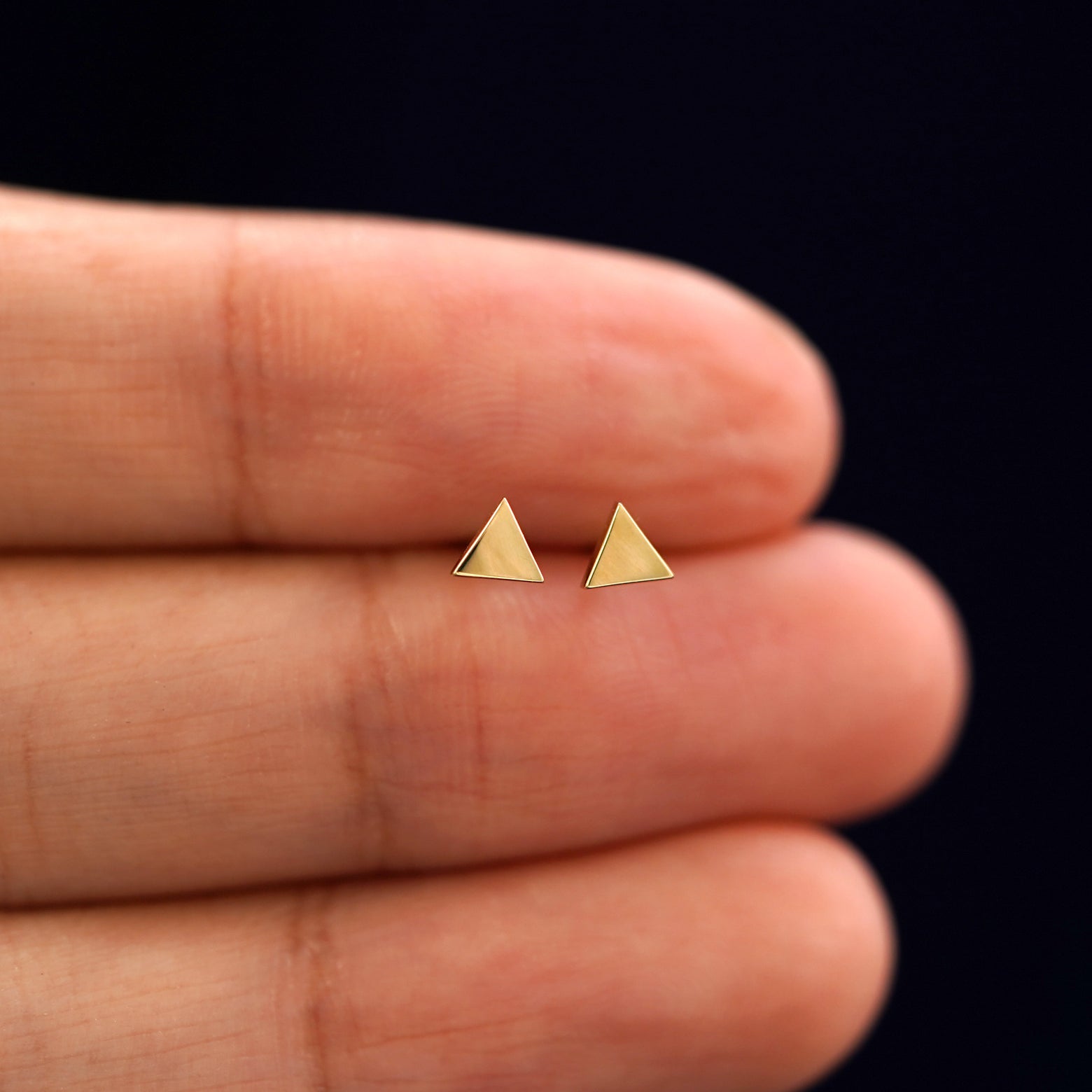 A model's hand holding a pair of recycled 14k gold Triangle Earrings