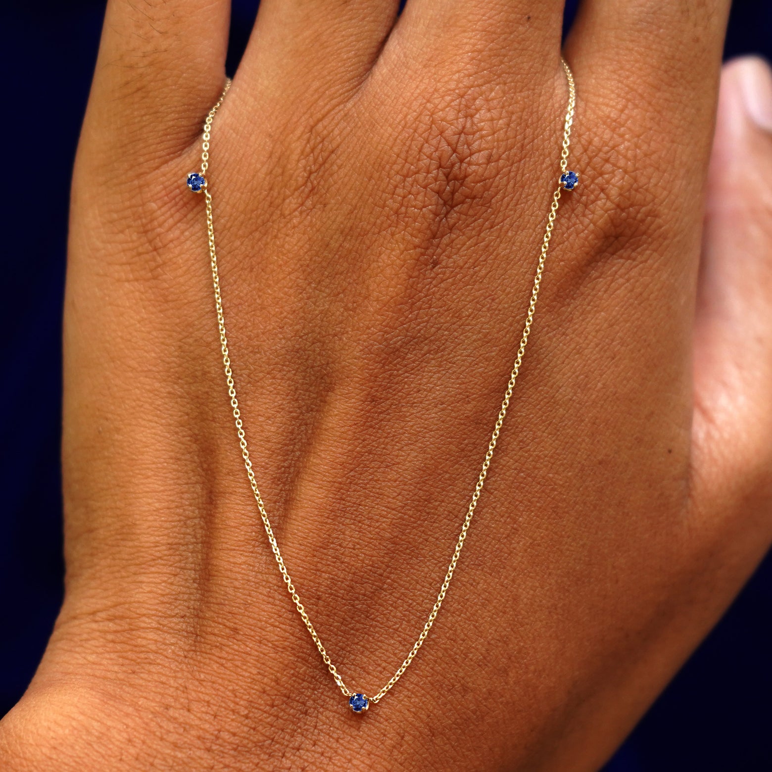 A solid gold sapphire 3 Gemstone Cable Necklace resting on the back of a model's hand