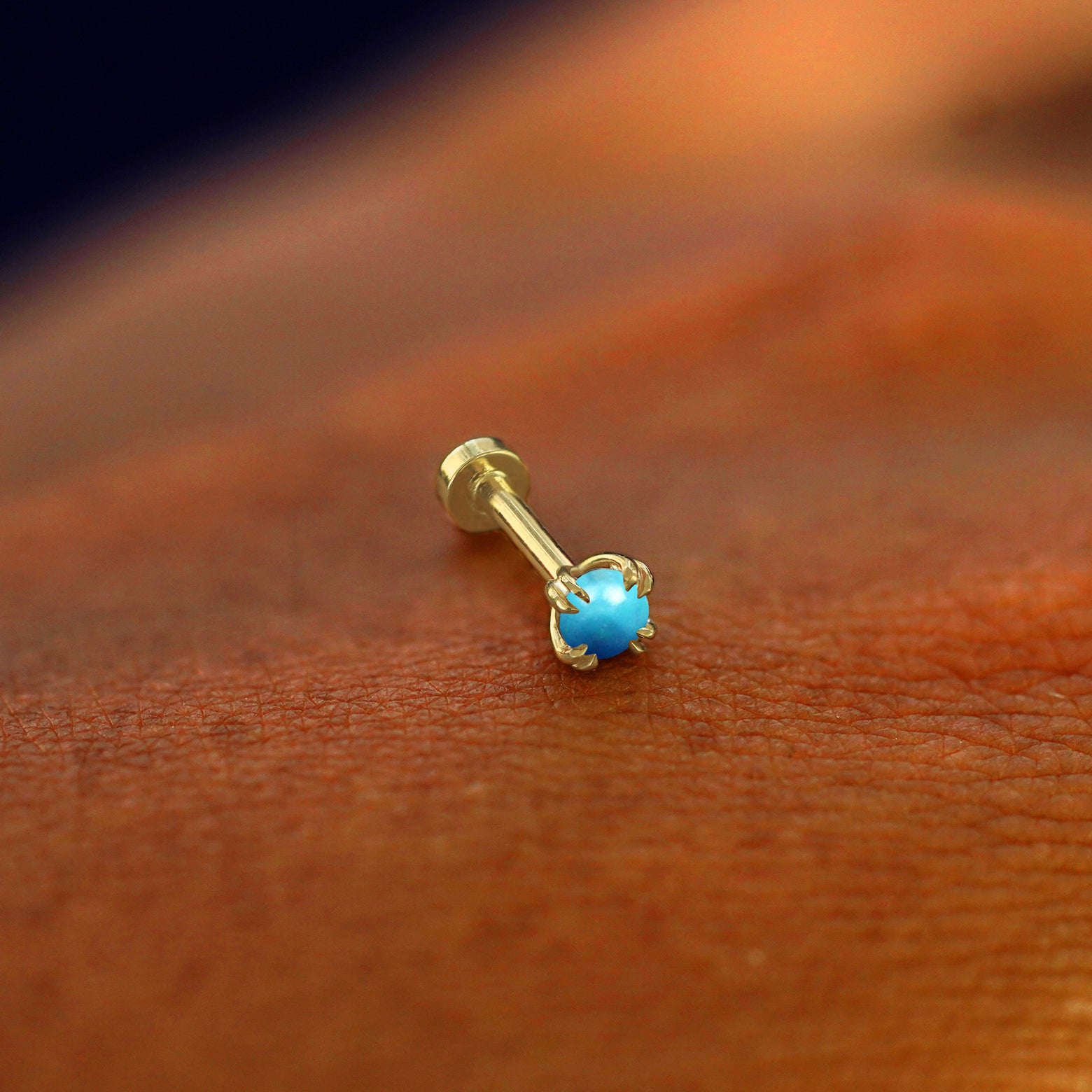 A solid 14k yellow gold Turquoise Flatback Piercing resting on the back of a model's hand