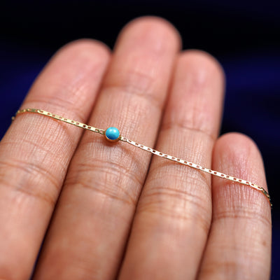 A yellow gold Turquoise Bracelet resting on a model's fingers