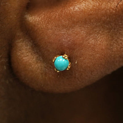 Close up view of a model's ear wearing a 14k yellow gold turquoise 3mm Gemstone Earring