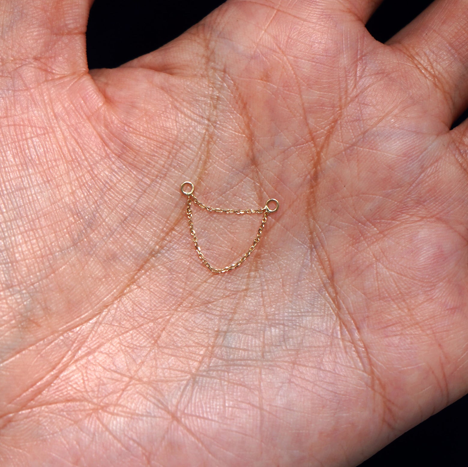 A solid 14k yellow gold Cable Chain Connector sitting in a model's hand