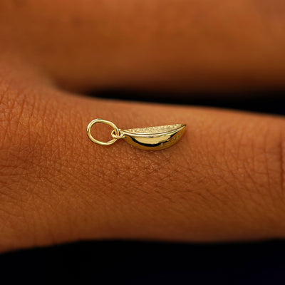 A 14k solid gold Watermelon Charm for chain balancing on the back of a model's finger