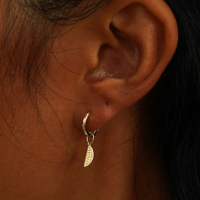 A model's ear wearing a yellow gold Watermelon Charm on a Curvy Huggie Hoop