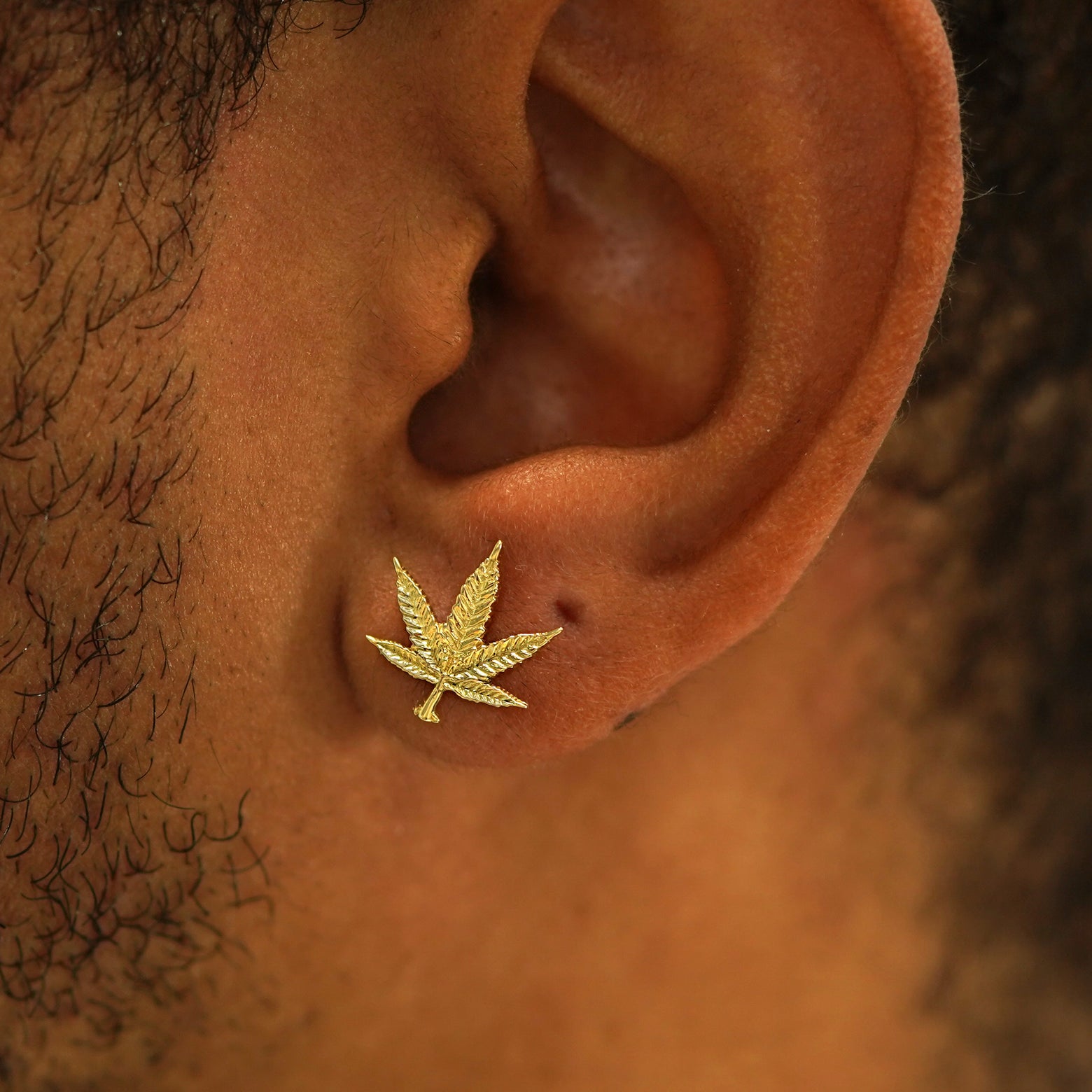 Close up view of a model's ear wearing a 14k gold Cannabis Earring