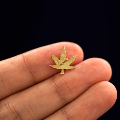 A yellow gold Cannabis Earring laying facedown on a model's fingers to show the underside view
