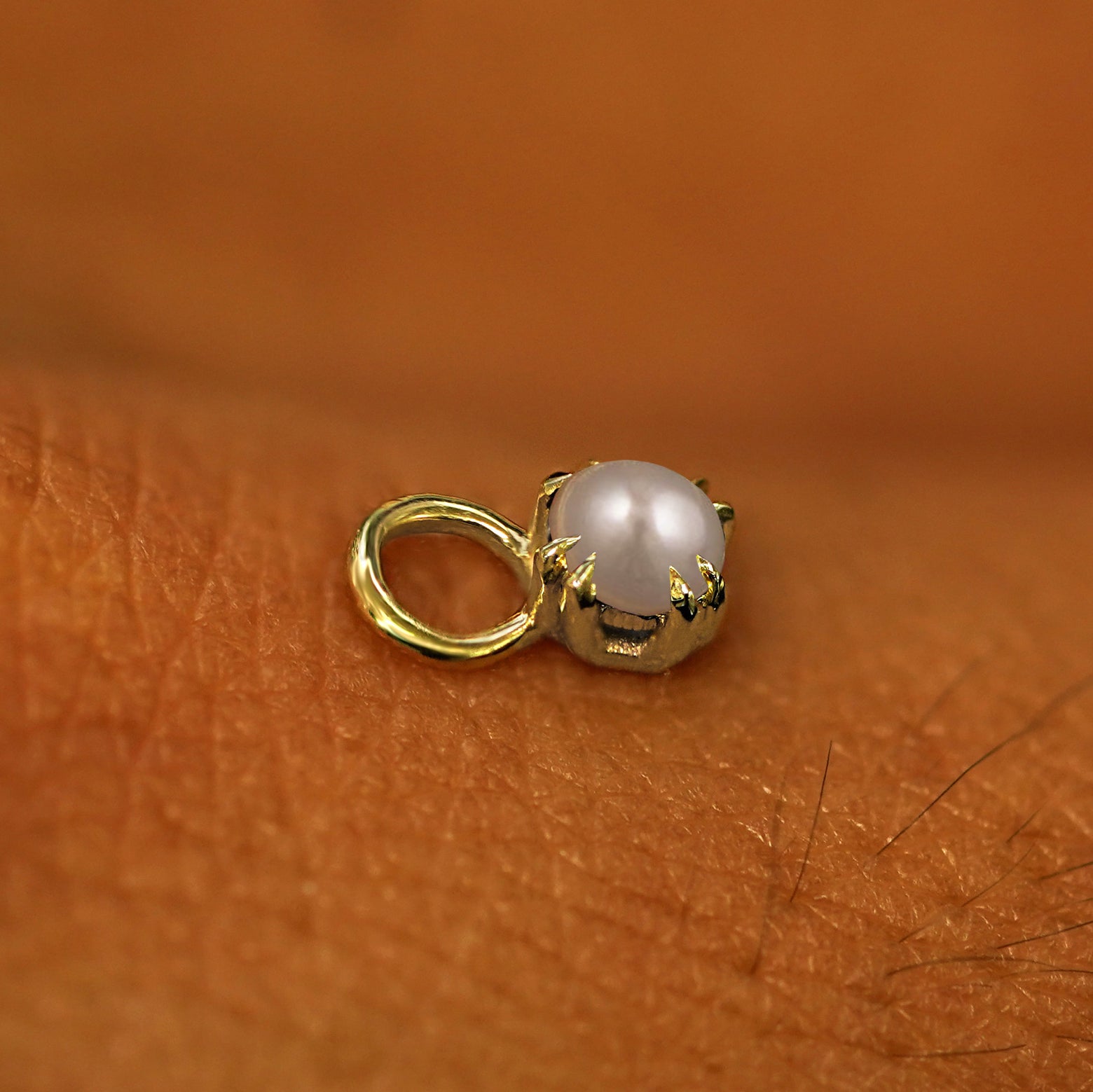 A solid yellow gold Pearl Charm for earring resting on the back of a model's hand