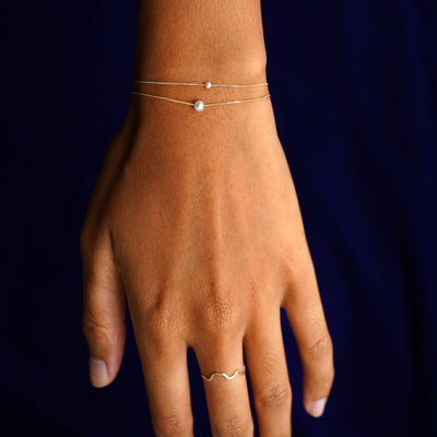 A model wearing both sizes of the Pearl Slide Bracelet layered from smallest to largest pearl and a yellow gold Wave Ring