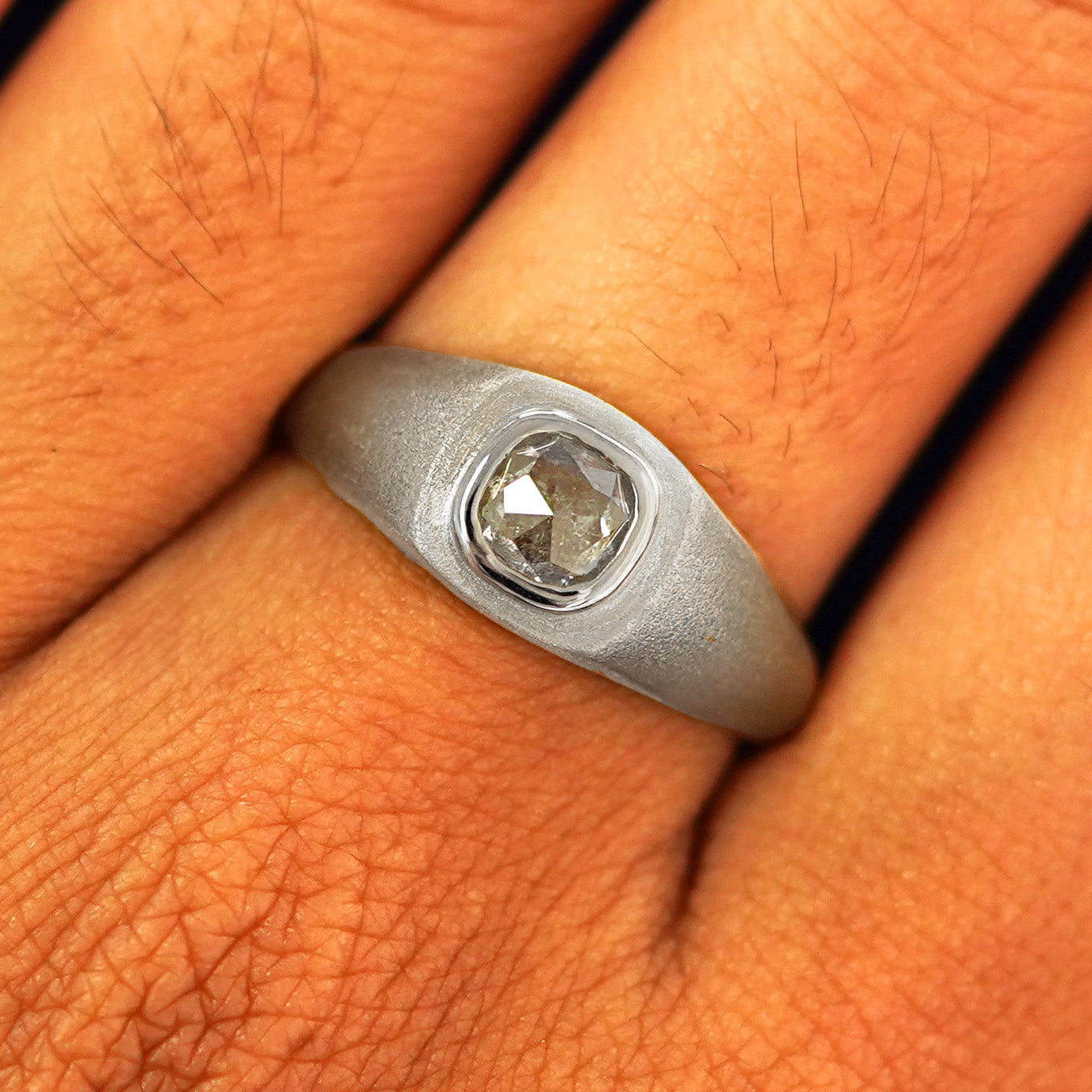 Close up view of a model's fingers wearing a 14k white gold Cushion Salt and Pepper Diamond Signet Ring