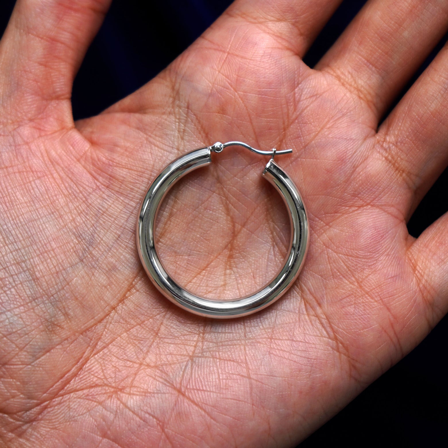 A solid 14k white gold Large Tube Hoop Earring closed in a model's palm