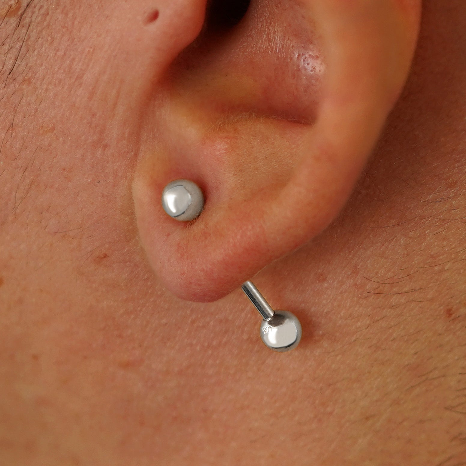 Close up view of a model's ear wearing a 14k white gold Medium Straight Barbell through a lobe piercing