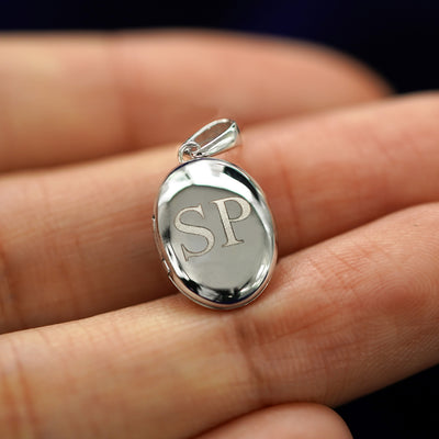 A 14k white gold Oval Locket Pendant with the initials SP engraved on the front resting on a model's fingers