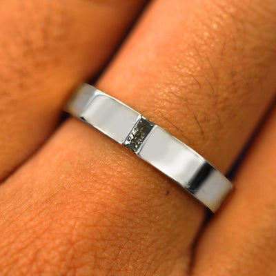 Close up view of a model's hand wearing a solid white gold Salt and Pepper Baguette Diamond Band