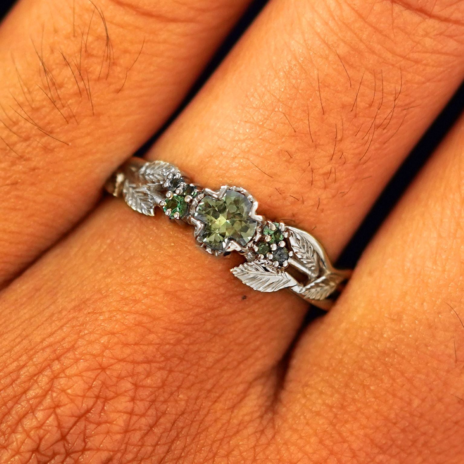 Close up view of a model's fingers wearing a 14k white gold Green Sapphire Leaves and Vines Ring