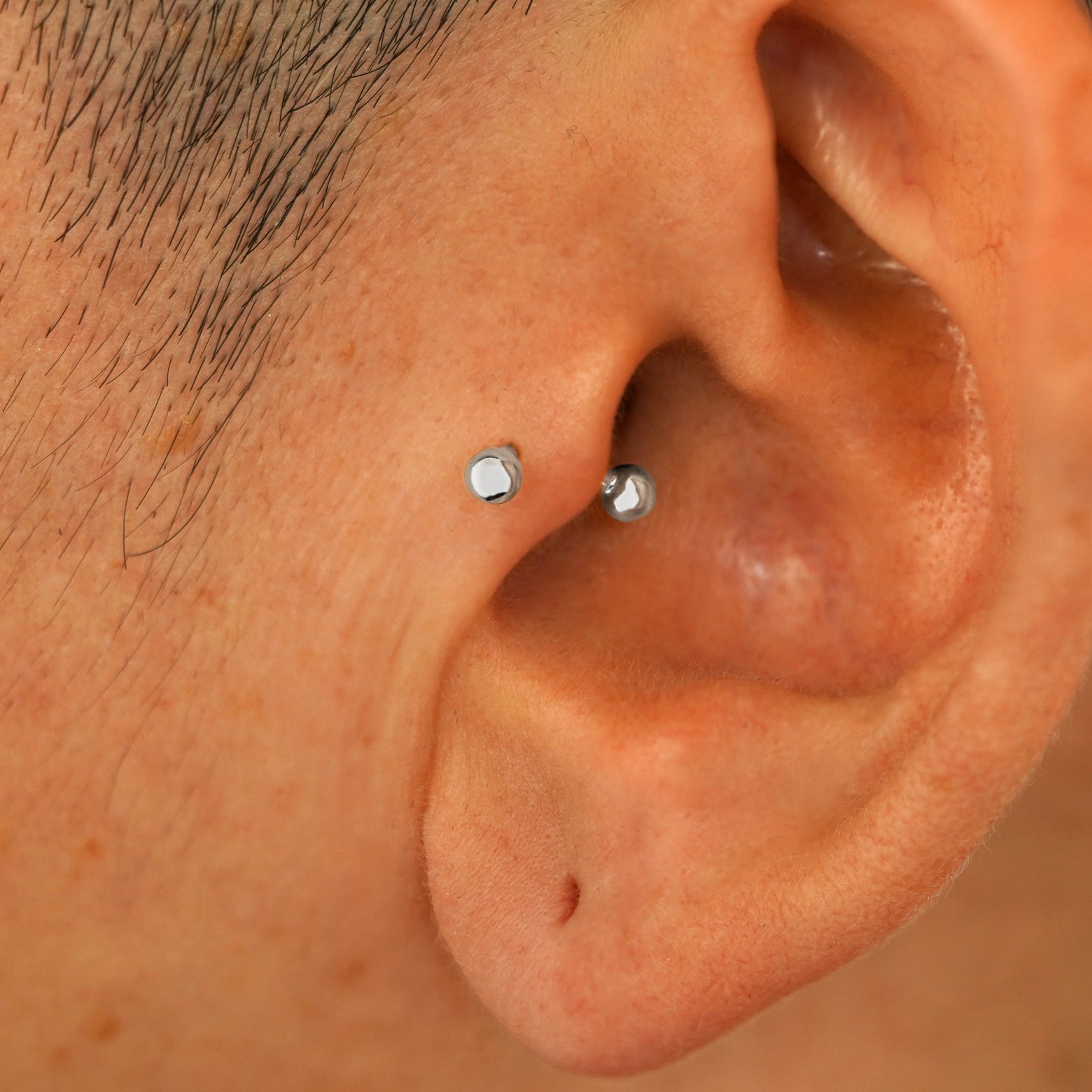 A model's ear wearing a white gold Small Curved Barbell in a tragus piercing