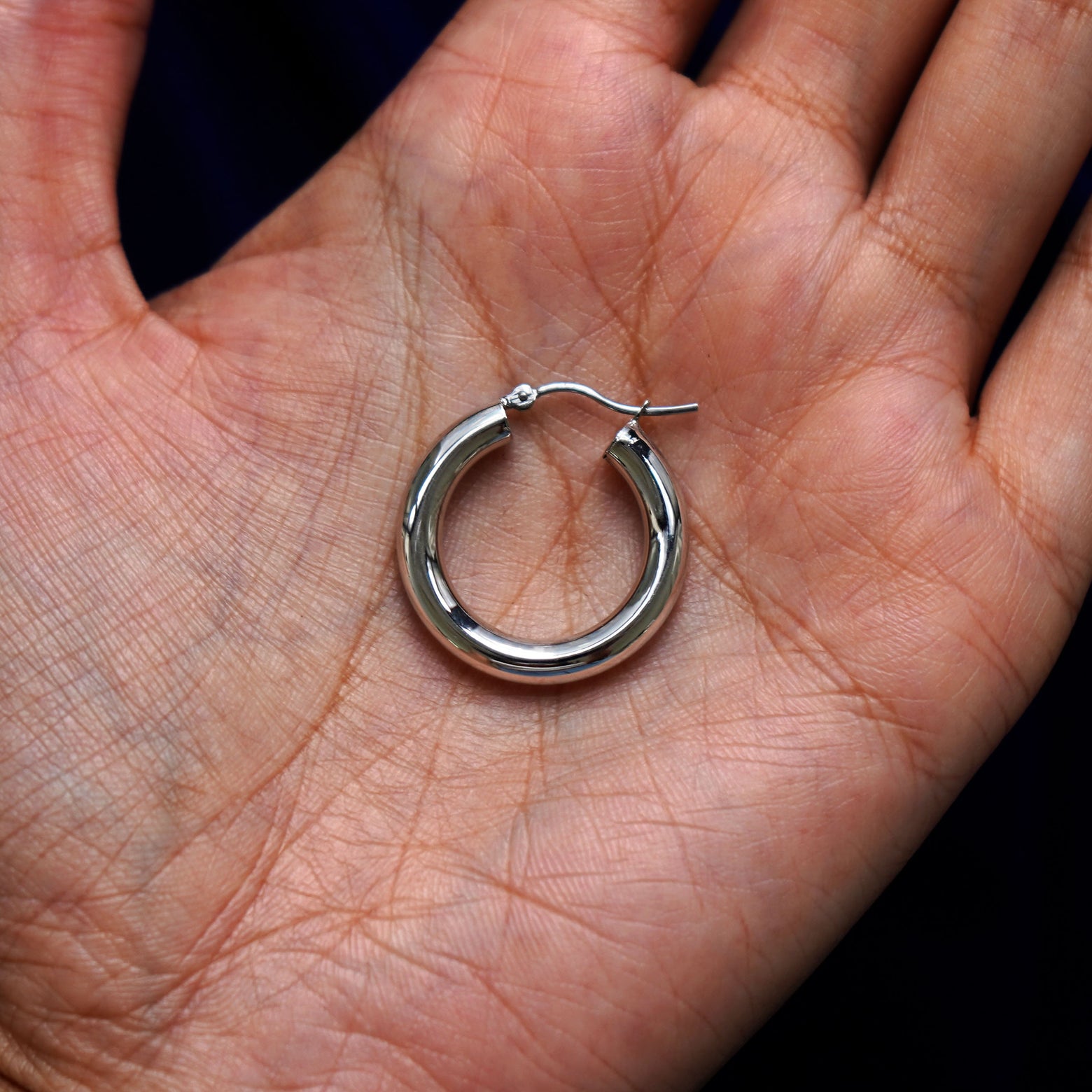 A solid 14k white gold Small Tube Hoop Earring closed in a model's palm