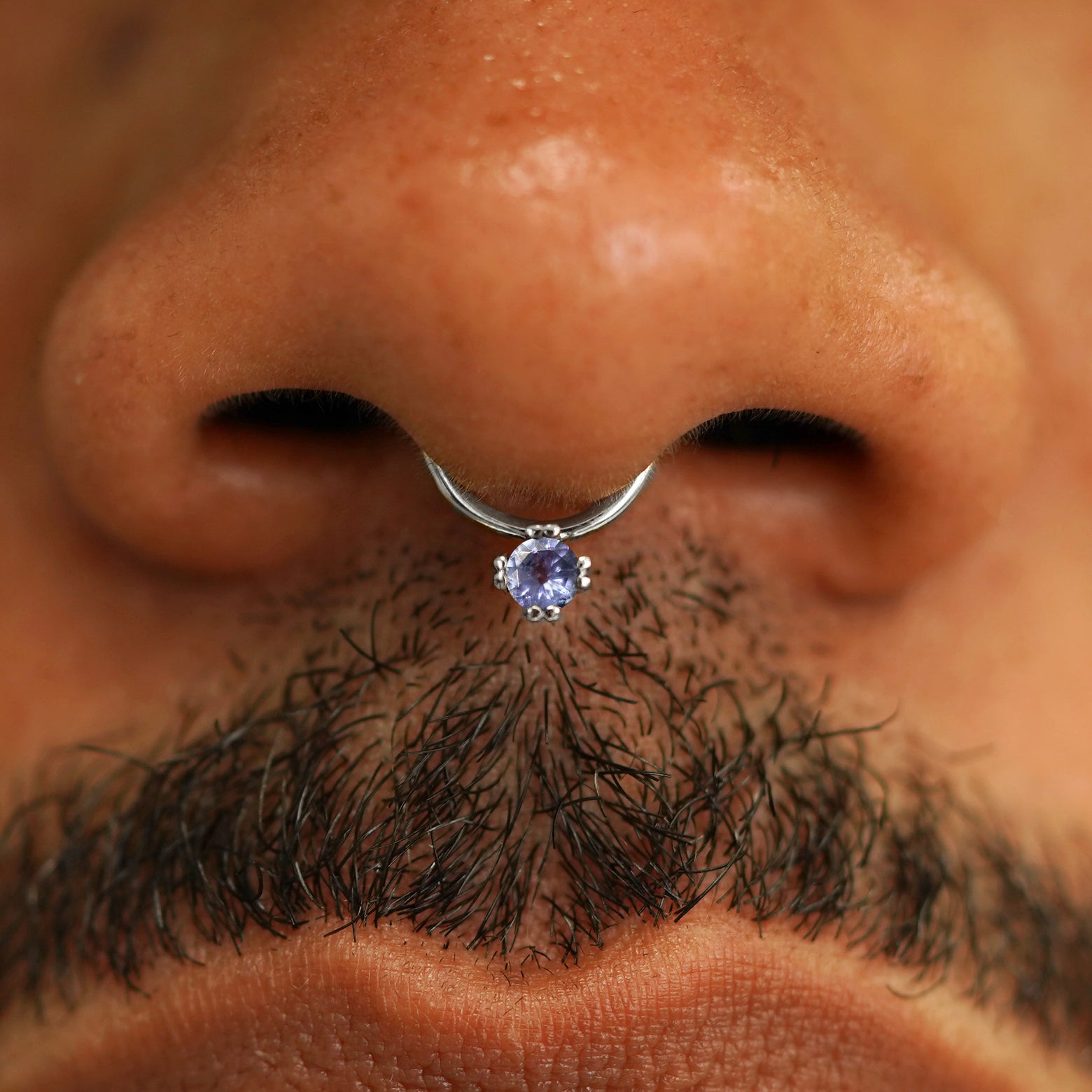 Close up view of a model's face wearing a 14k solid white gold tanzanite Gemstone Septum