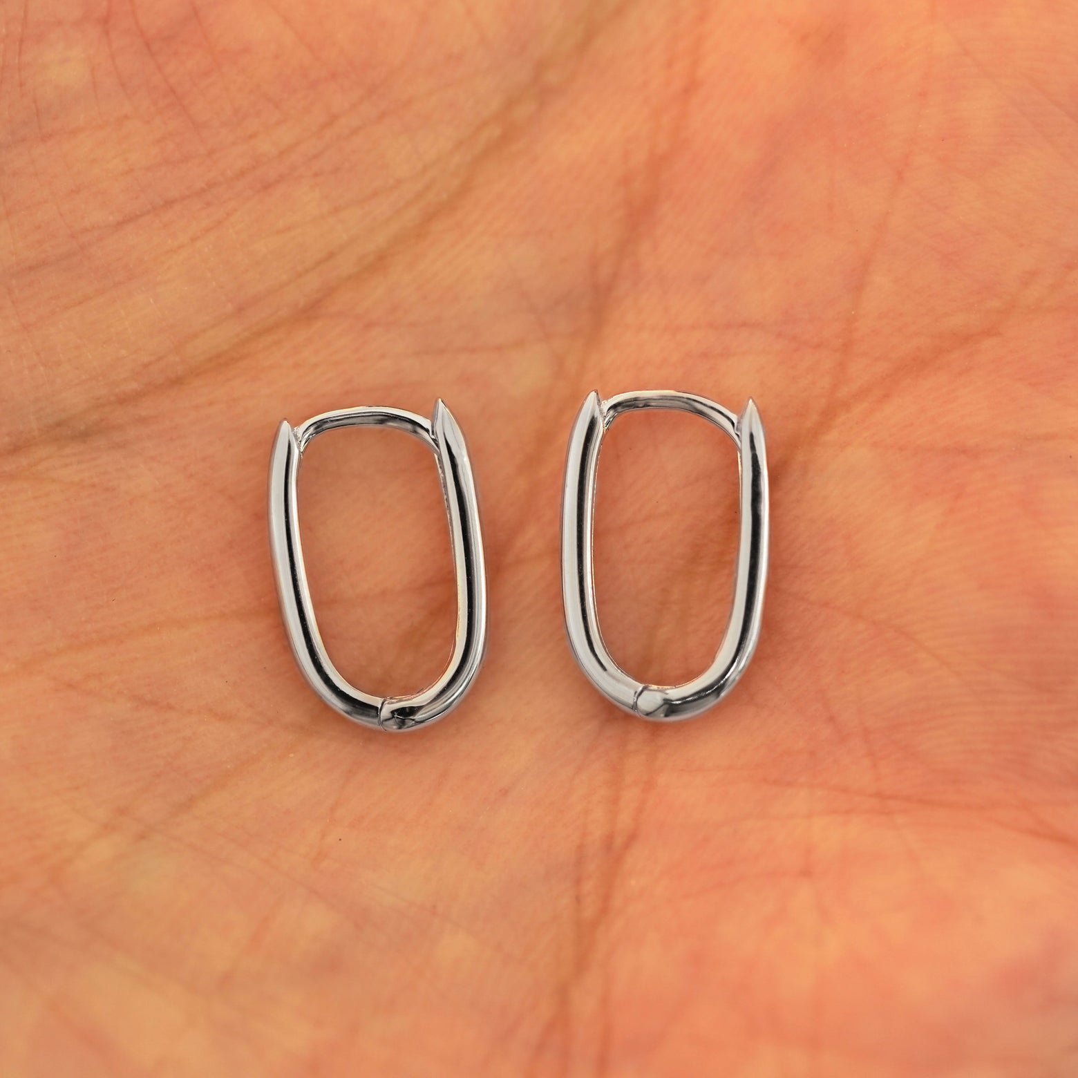 A pair of 14k white gold Thin Oval Huggie Hoops resting in a model's palm