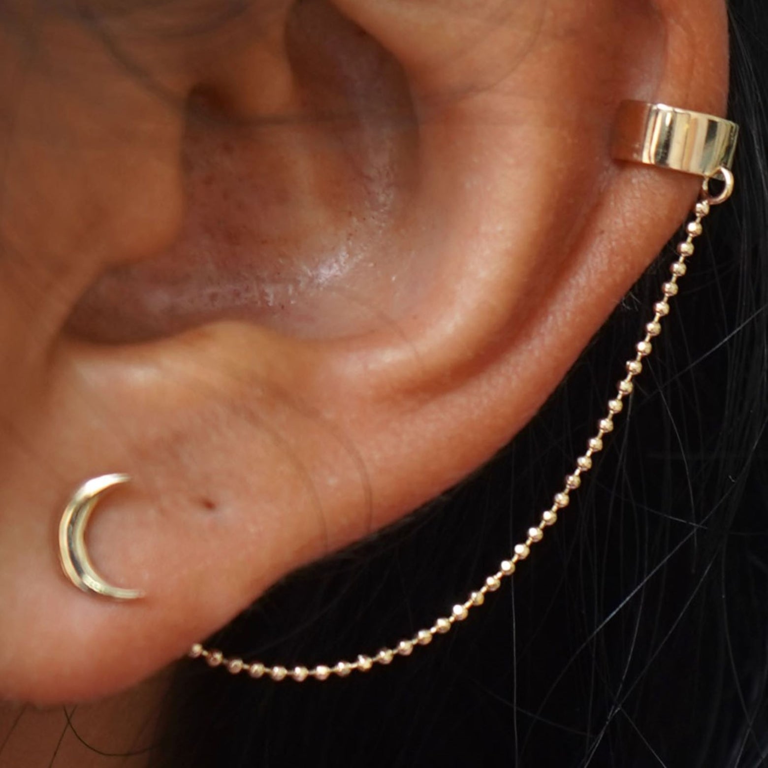 Close up view of a model's ear wearing a yellow gold Thick Cuff With Chain and a Moon Earring