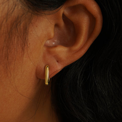 A model's ear wearing a 14 karat yellow gold Thick Oval Huggie Hoop