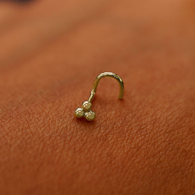 A yellow gold Ball Trio Nose Stud laying on the back of a model's hand