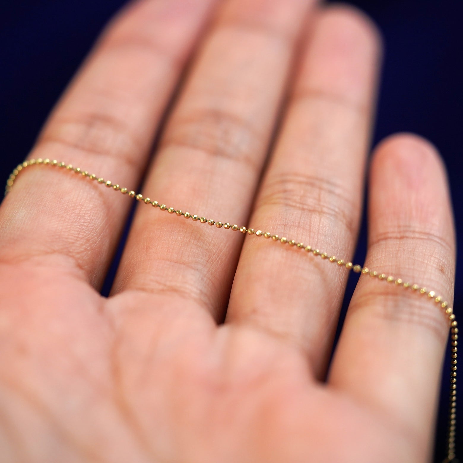 A yellow gold Bead Necklace resting on a model's fingers