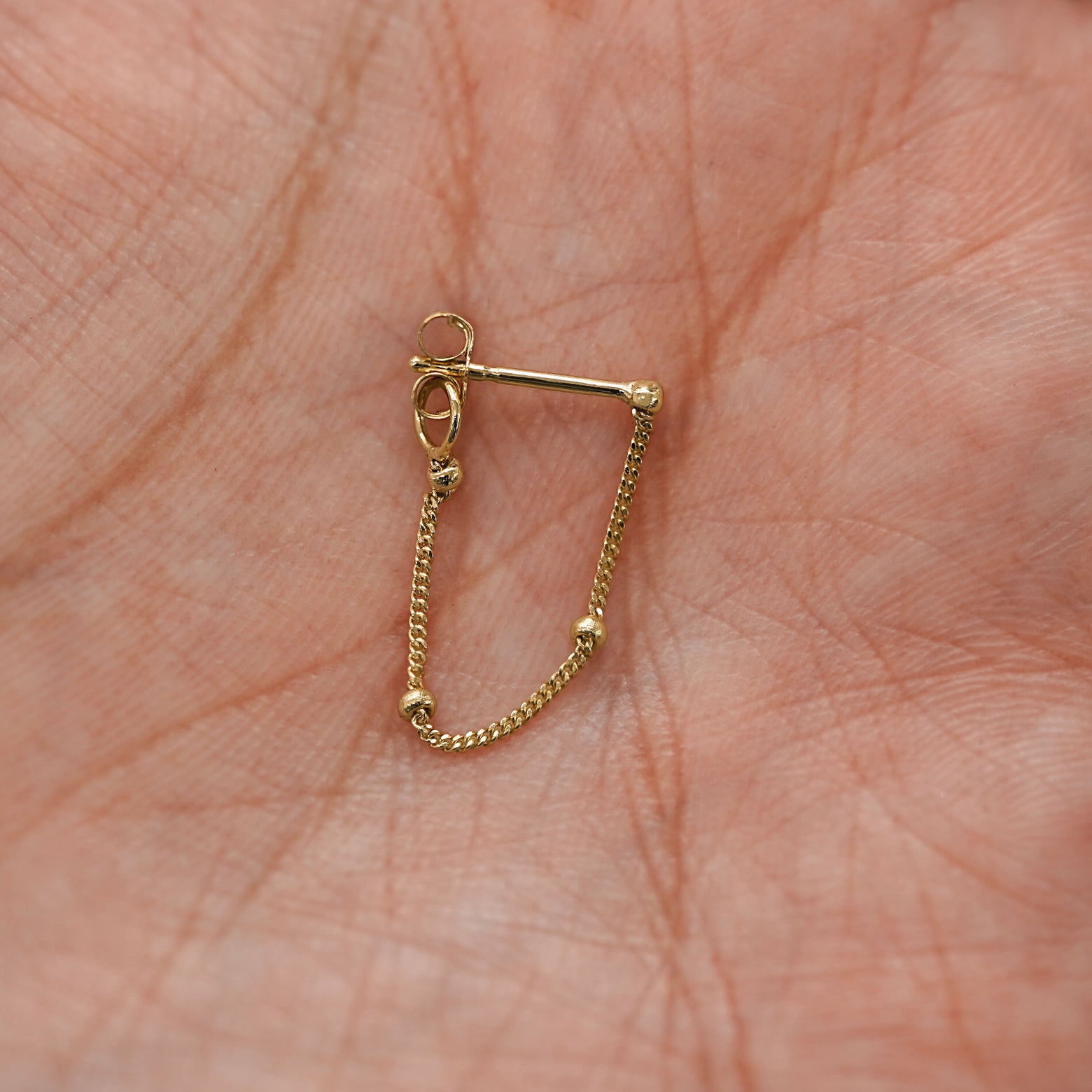 A yellow gold Beaded Chain Loop Earring in model's palm