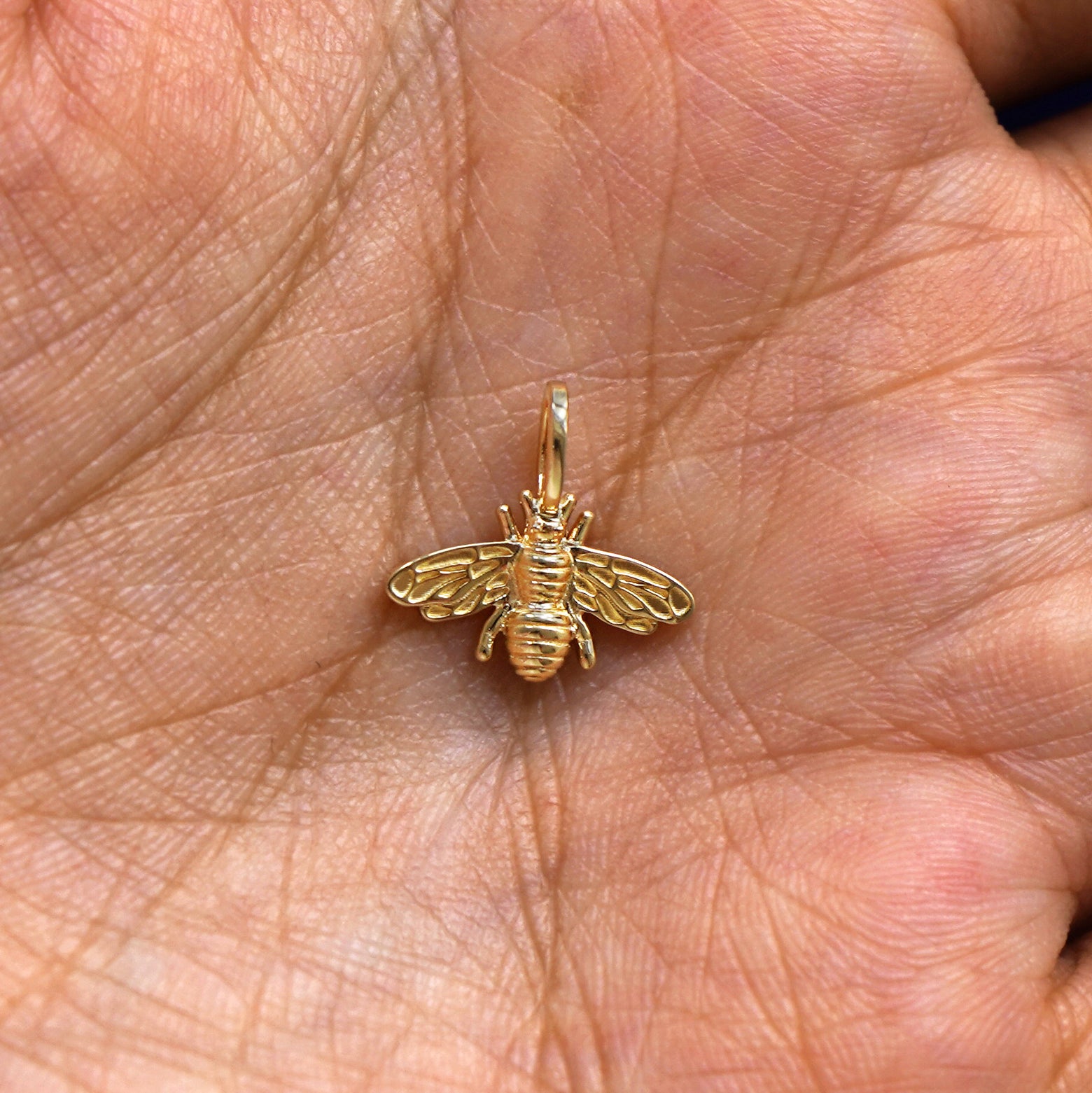 A solid gold Bee Charm for chain resting in a model's palm