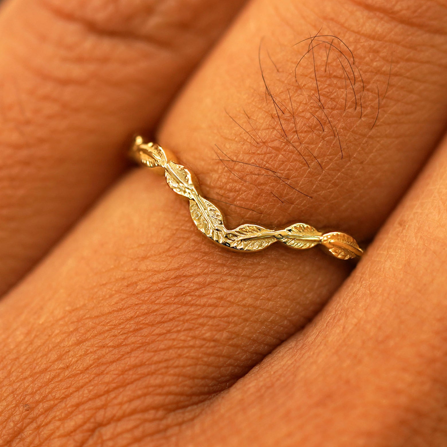 Close up view of a model's fingers wearing a 14k yellow gold Chevron Leaves Band