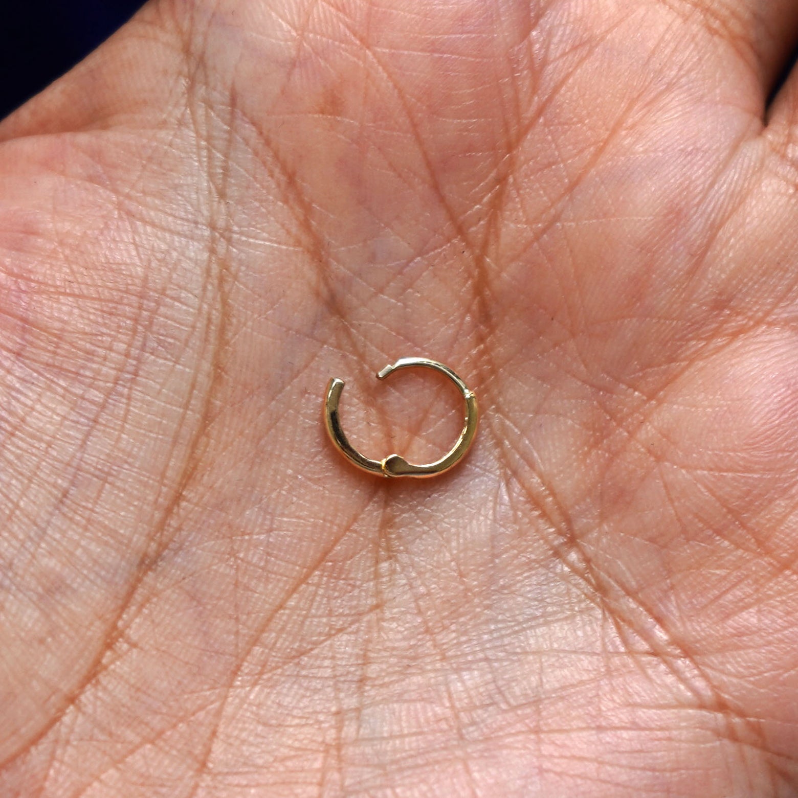 A solid 14k yellow gold Small Curvy Huggie Hoop Earring open in a model's palm to show the hinge
