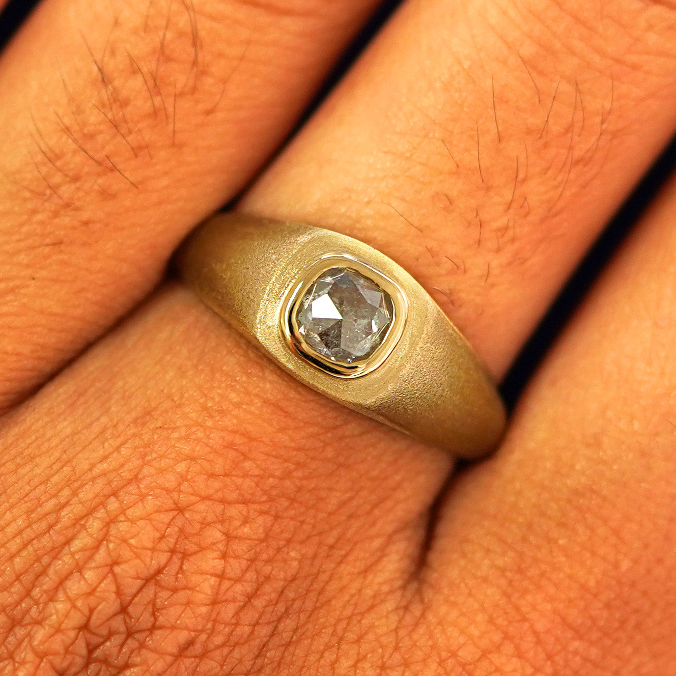 Close up view of a model's fingers wearing a 14k yellow gold Cushion Salt and Pepper Diamond Signet Ring