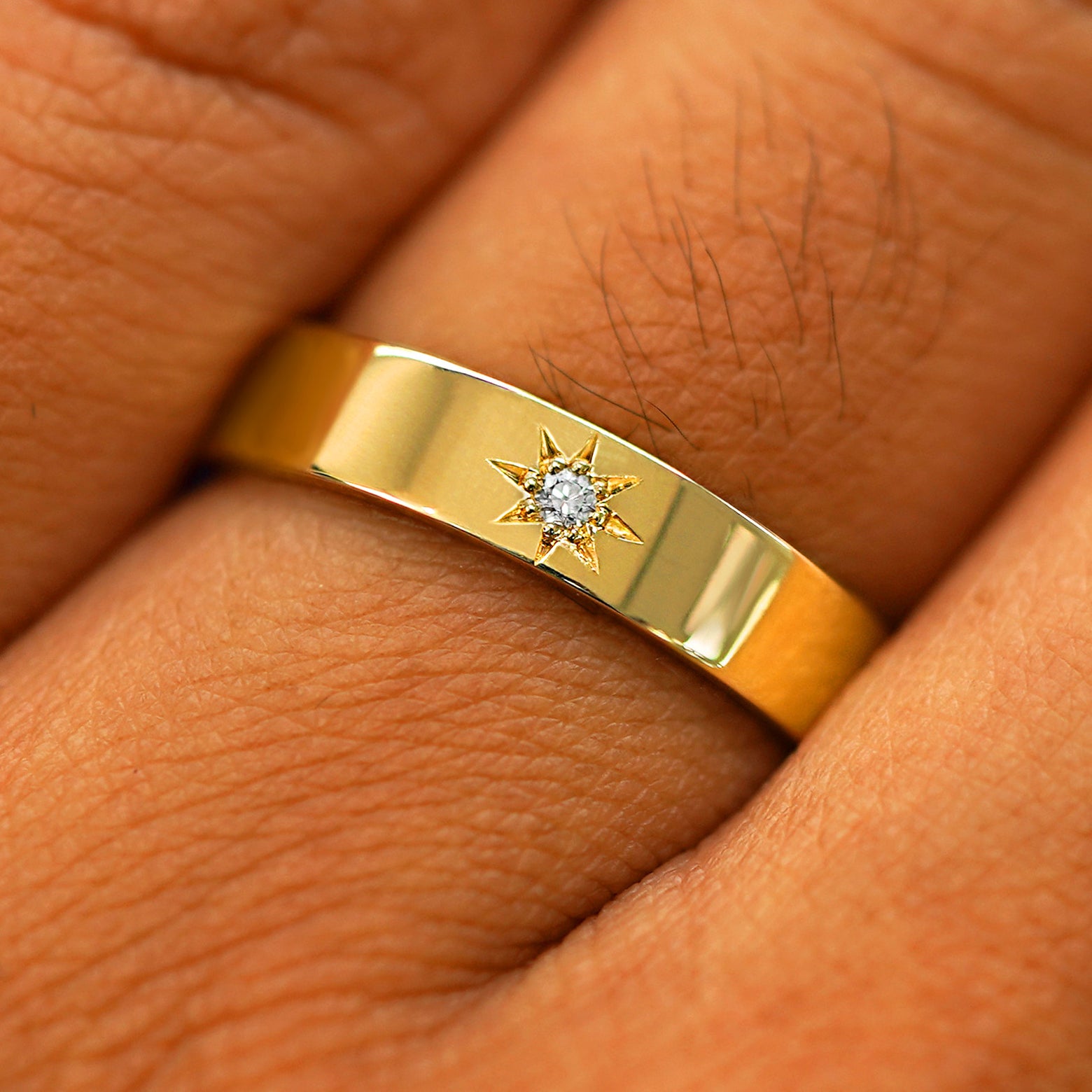 Close up view of a model's hand wearing a solid yellow gold Engraved Star Diamond Band