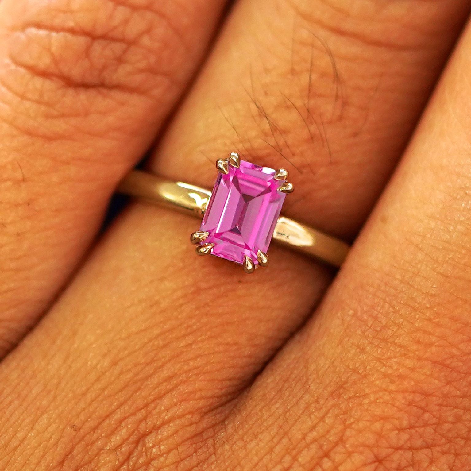 Close up view of a model's fingers wearing a 14k yellow gold Emerald Cut Pink Sapphire Ring