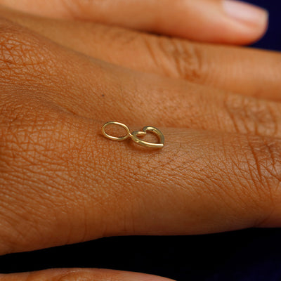 A 14k yellow gold Heart Charm for chain balancing on the back of a model's finger