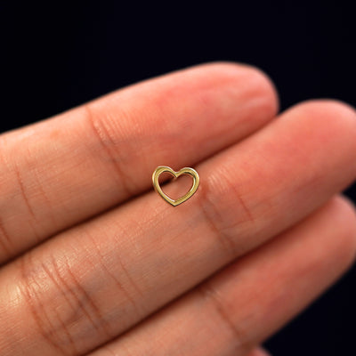 A solid 14k yellow gold Heart Earring in between a model's fingers