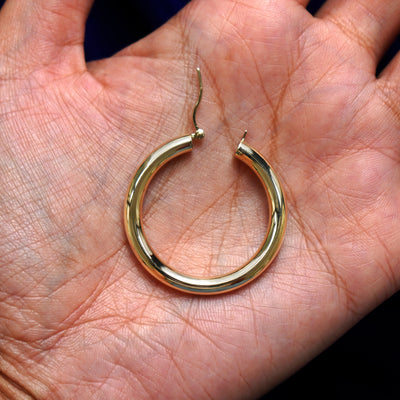 A solid 14k yellow gold Large Tube Hoop Earring open in a model's palm to show the hinge