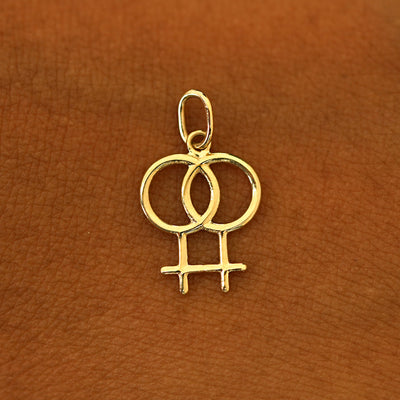 A solid 14k  yellow gold Lesbian Symbol Charm resting on the back of a model's hand