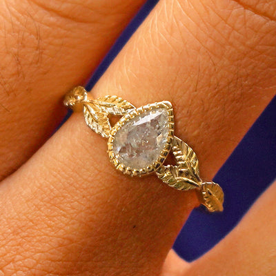 Close up view of a model's fingers wearing a 14k yellow gold Pear Salt and Pepper Diamond Leaves Ring