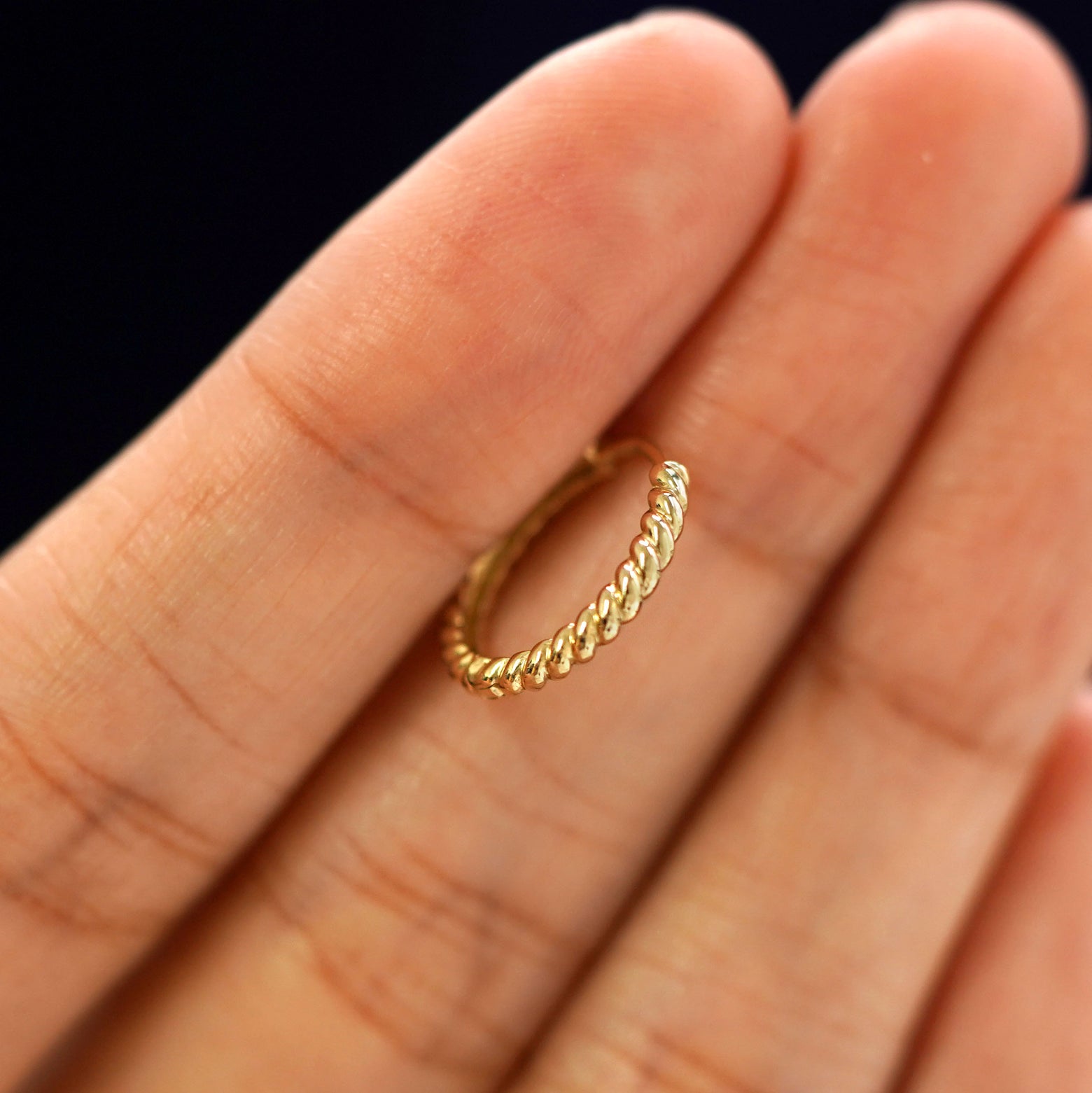 A 14k gold Medium Rope Huggie Hoop Earring held in between a model's fingers to show the hoops thickness