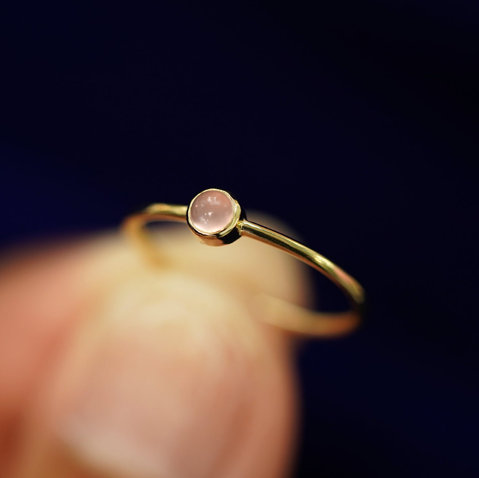 A model holding a 14k gold Rose Quartz Ring between their fingers to show the details of the bezel set stone