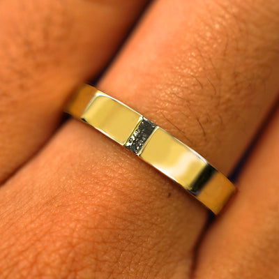 Close up view of a model's hand wearing a solid yellow gold Salt and Pepper Baguette Diamond Band