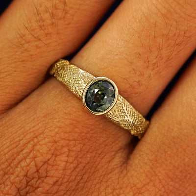 Close up view of a model's fingers wearing a 14k yellow gold Dark Green Sapphire Pine Ring