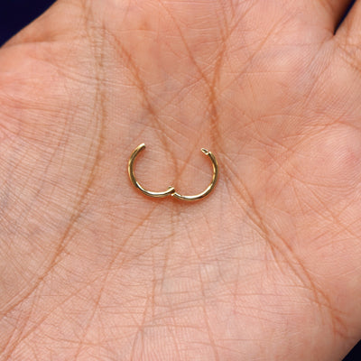 A 14 karat solid gold Small Seamless Huggie Hoop / Piercing open to show hinge closure resting in a model's palm
