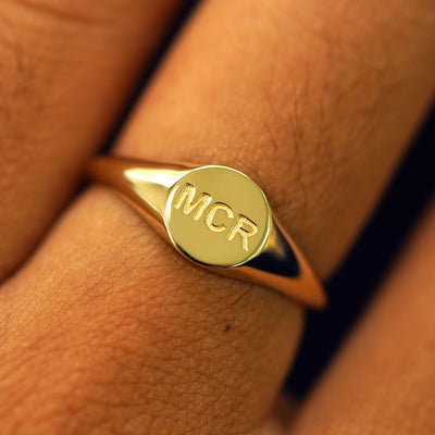 A yellow gold Signet Ring on a model's finger with the initials MCR Z engraved on top in a classic block font