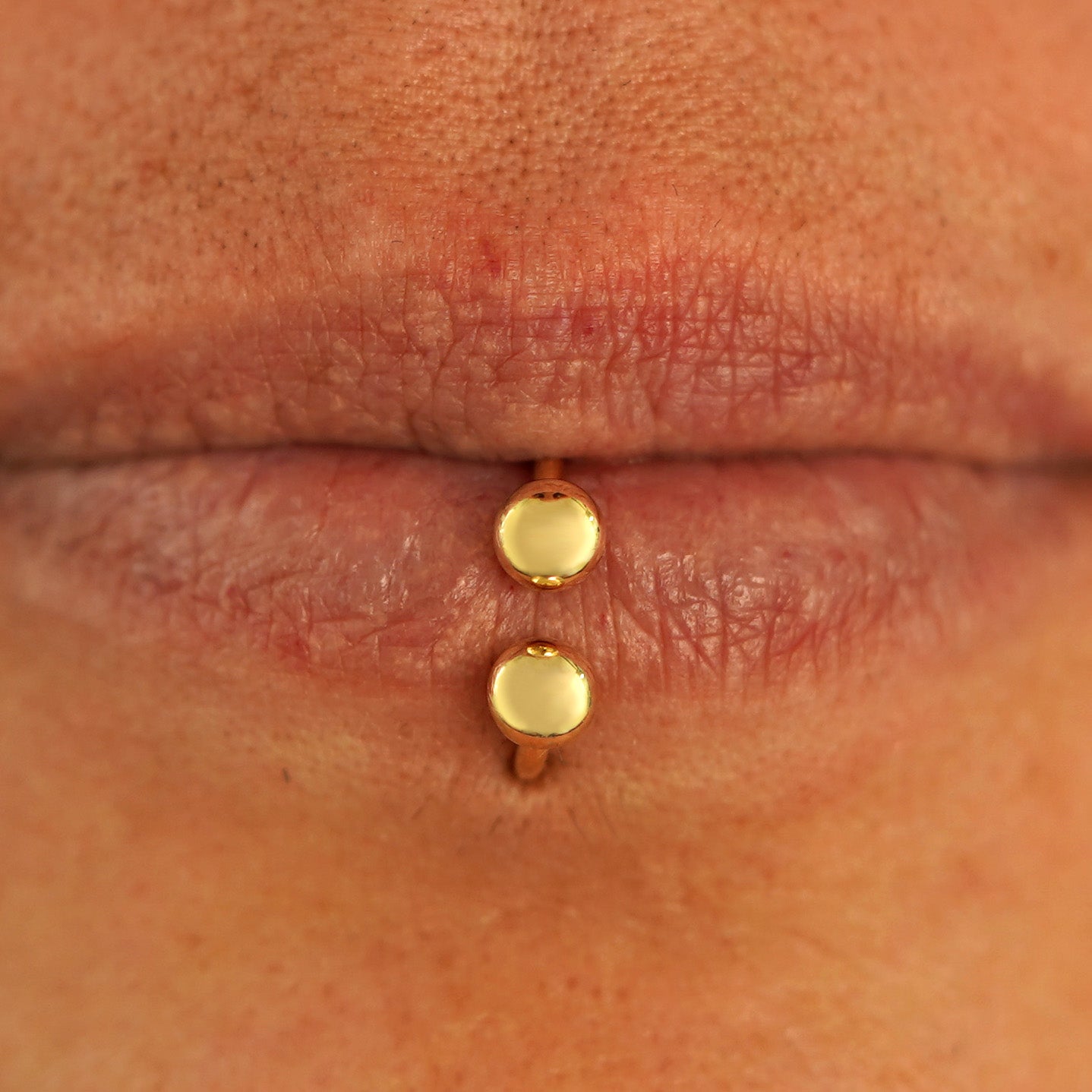 Close up view of a model's lips wearing a 14k yellow gold Small Horseshoe as a lip ring through a labret piercing