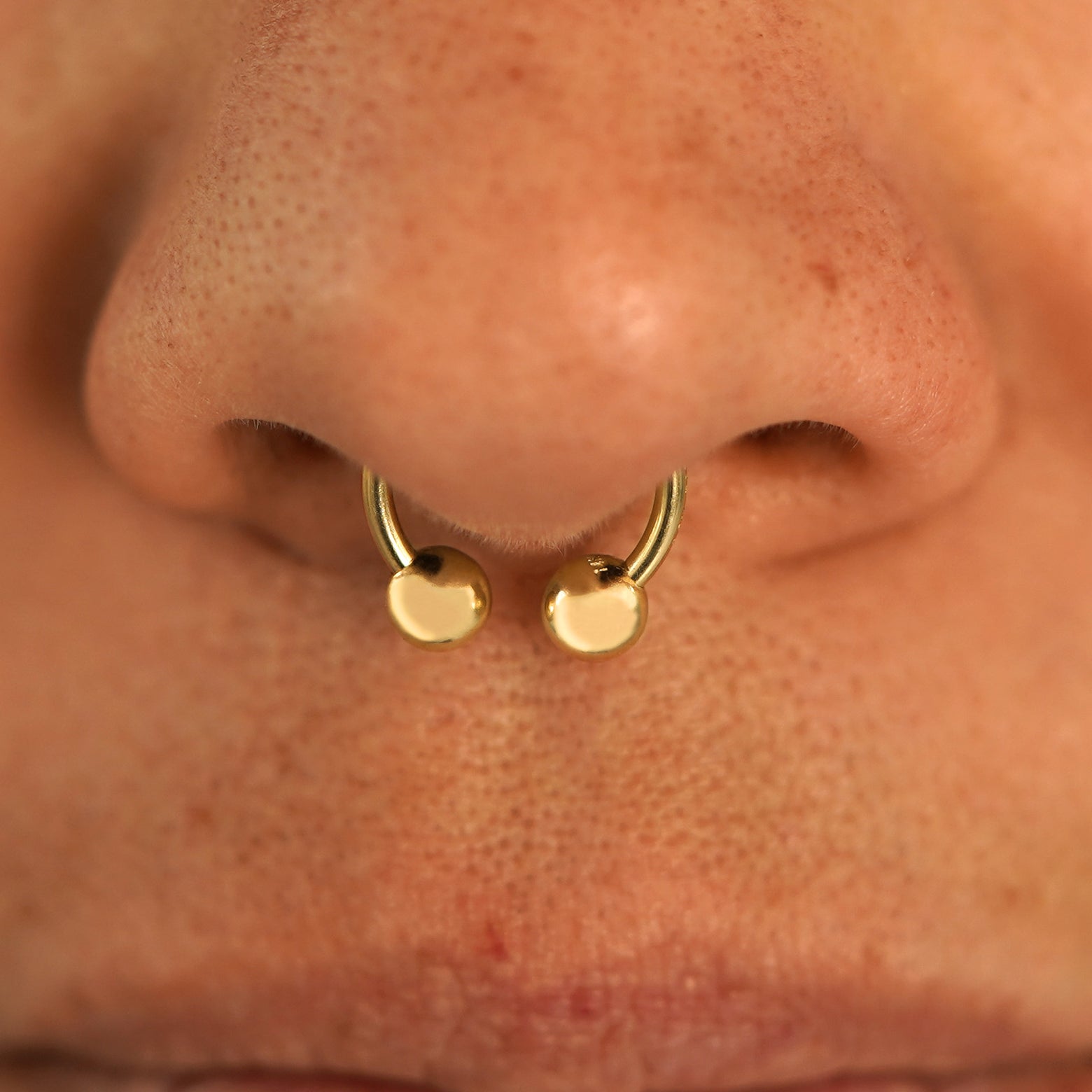 Close up view of a model's nose wearing a 14k yellow gold Small Horseshoe in a septum piercing