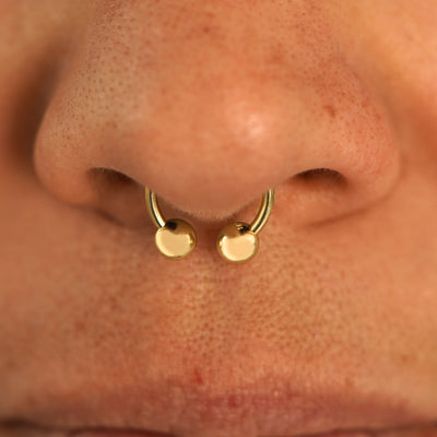 Close up view of a model's nose wearing a 14k yellow gold Small Horseshoe in a septum piercing