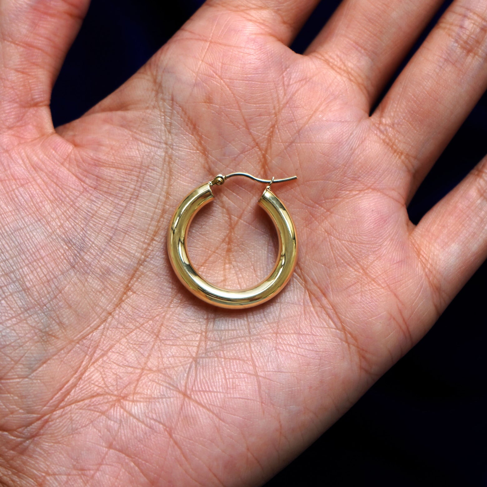 A solid 14k yellow gold Small Tube Hoop Earring closed in a model's palm