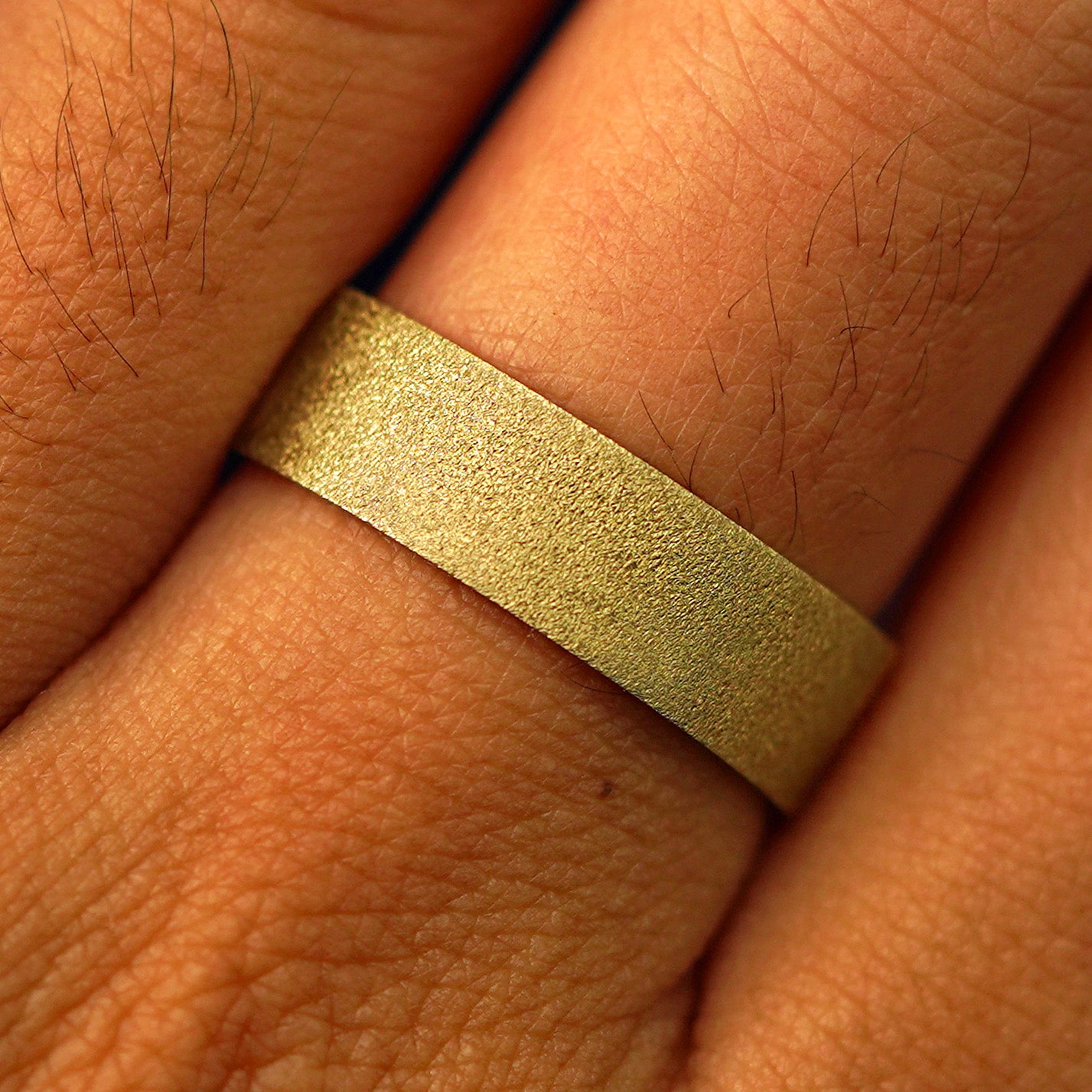 Close up view of a model's fingers wearing a 14k yellow gold Industrial Stardust Band