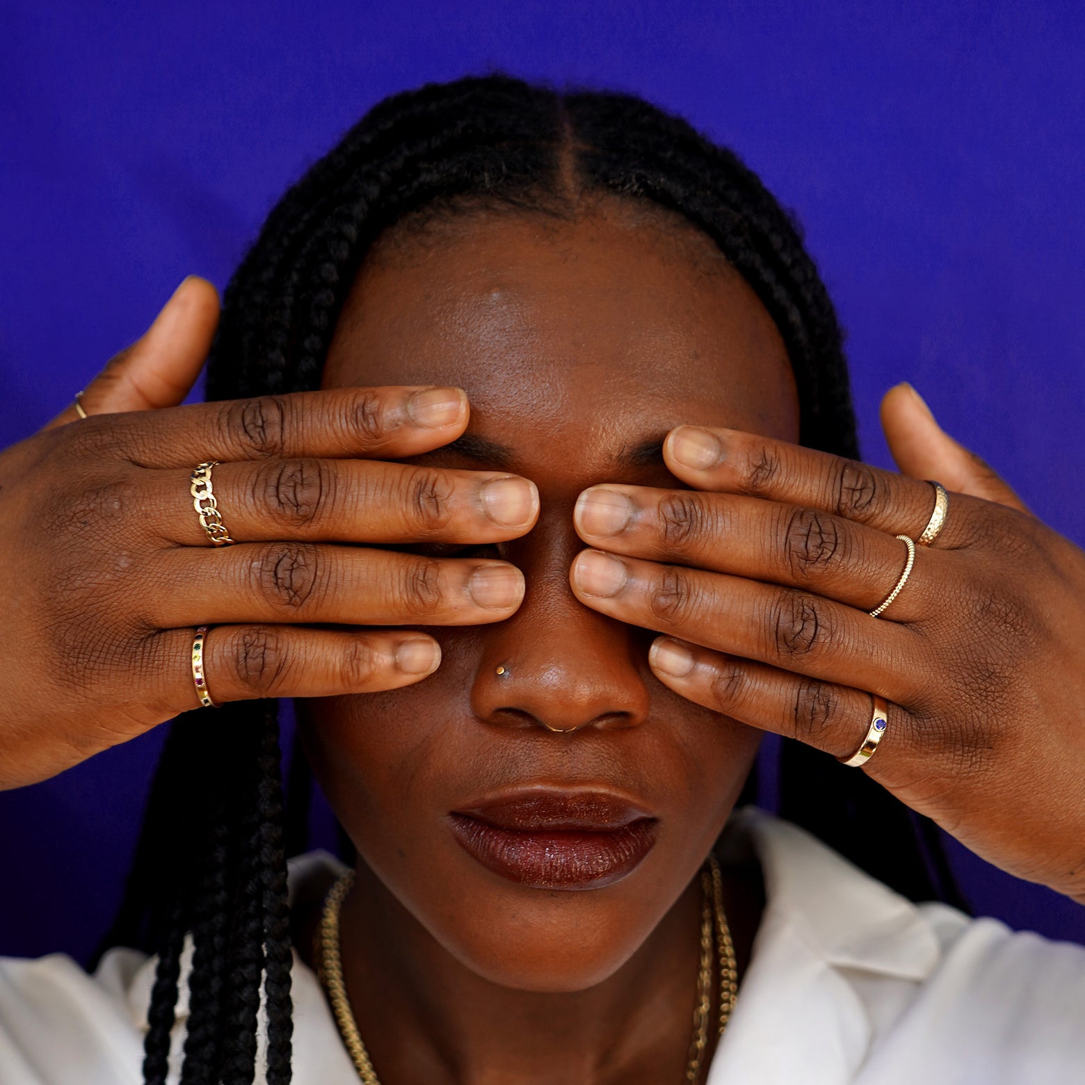 A model covering their eyes with their finger tips wearing various yellow gold Automic Gold rings